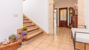 Un escalier orné de carreaux décoratifs, un banc en bois et un lit dans un couloir dont le sol est carrelé et les murs sont en pierre.