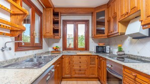 Une cuisine avec des meubles en bois, un plan de travail en granit, un évier, un four à micro-ondes et une fenêtre donnant sur un paysage verdoyant.