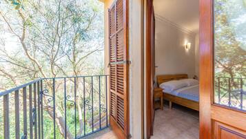 A balcony with a wooden door, a bed with a wooden headboard, and a small table.