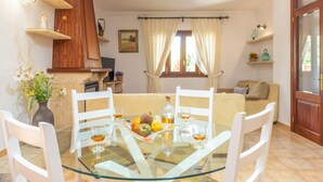 Un coin repas avec une table en verre, des chaises blanches, une assiette de fruits et une bouteille de vin.