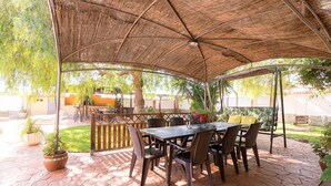 Eine Außenpatio mit Tisch und Stühlen unter einem gewebten Baldachin, umgeben von Topfpflanzen und einem steinbelagten Boden.