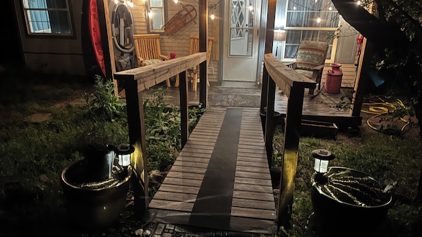 Une terrasse en bois qui mène à un espace extérieur abrité, aménagé avec des sièges et doté d’une porte.