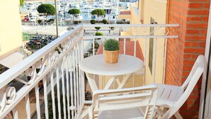 Ein Balkon mit weißen Stühlen und einem kleinen Tisch, mit Blick auf eine Marina und Boote.