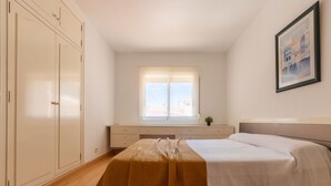Ein Schlafzimmer mit Bett, Fenster, Kommode und einem Bild an der Wand.