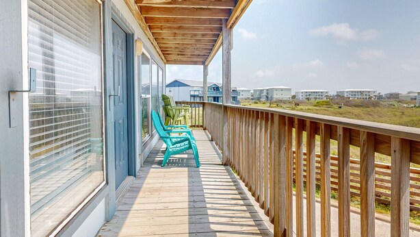 Une terrasse en bois avec un espace couvert, une porte bleue et une vue sur un quartier résidentiel.