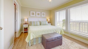 Une chambre à coucher comprenant un lit, une table de chevet, une lampe, un ventilateur de plafond et une fenêtre avec des stores.