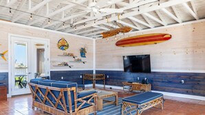 Une pièce spacieuse avec un plafond haut, un grand téléviseur fixé au mur et une décoration sur le thème du surf.