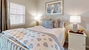 A bedroom with a bed, two bedside tables, a window with blinds, and a framed picture on the wall. - Shared Pool and Hot Tub, Golf Cart Access (Port Aransas)