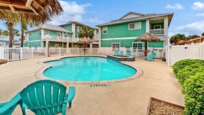 A pool area with a curved pool, a thatched umbrella, and a two-story building with balconies. - Shared Pool and Hot Tub, Golf Cart Access (Port Aransas)