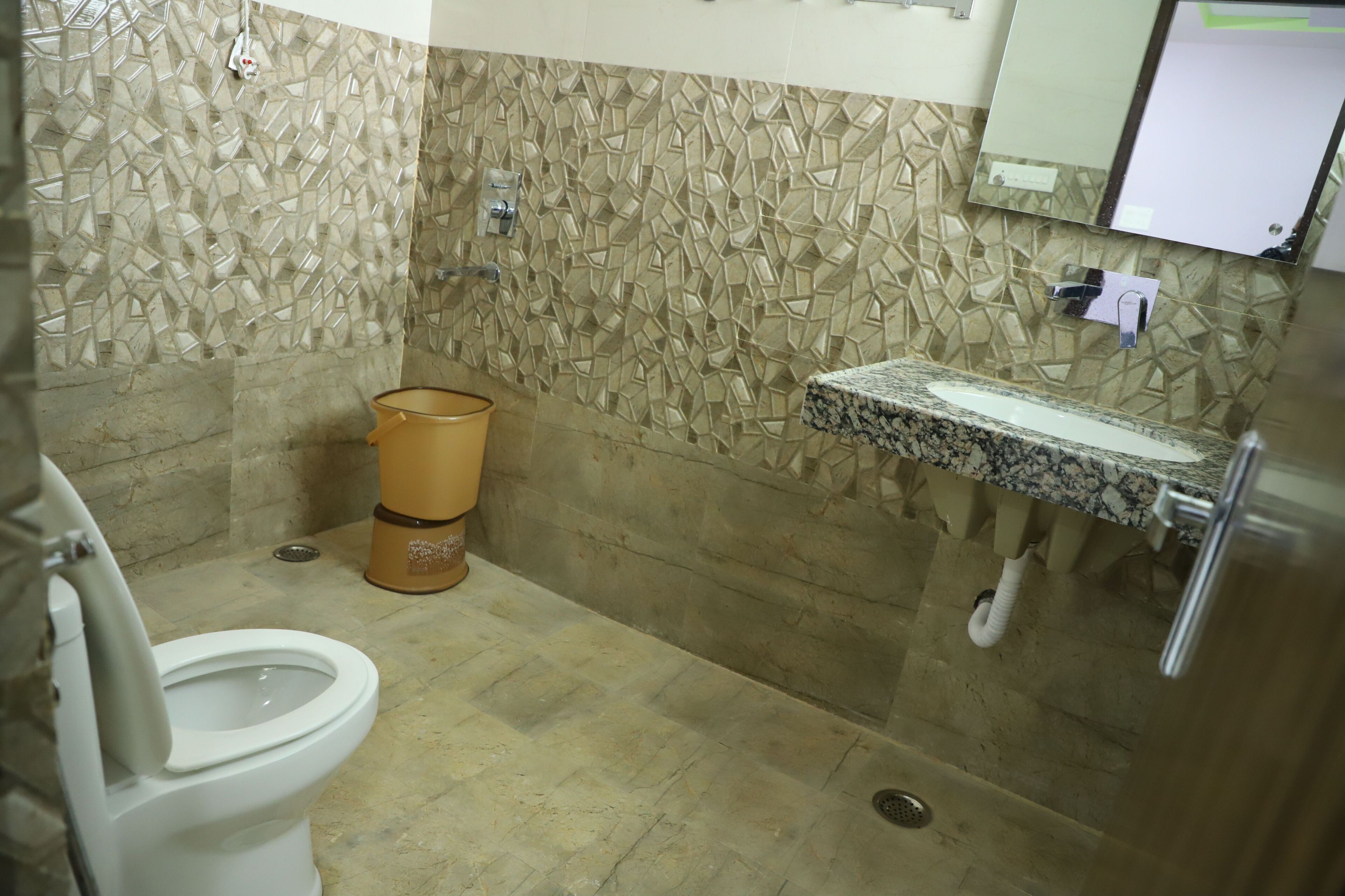 Een badkamer met een wand van mozaïektegels, een toilet, een wastafel met een marmeren blad en een prullenbak.