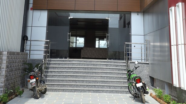 La entrada al Hotel Amar Palace, con una fachada moderna, una escalera que conduce a la entrada y dos motocicletas estacionadas afuera.