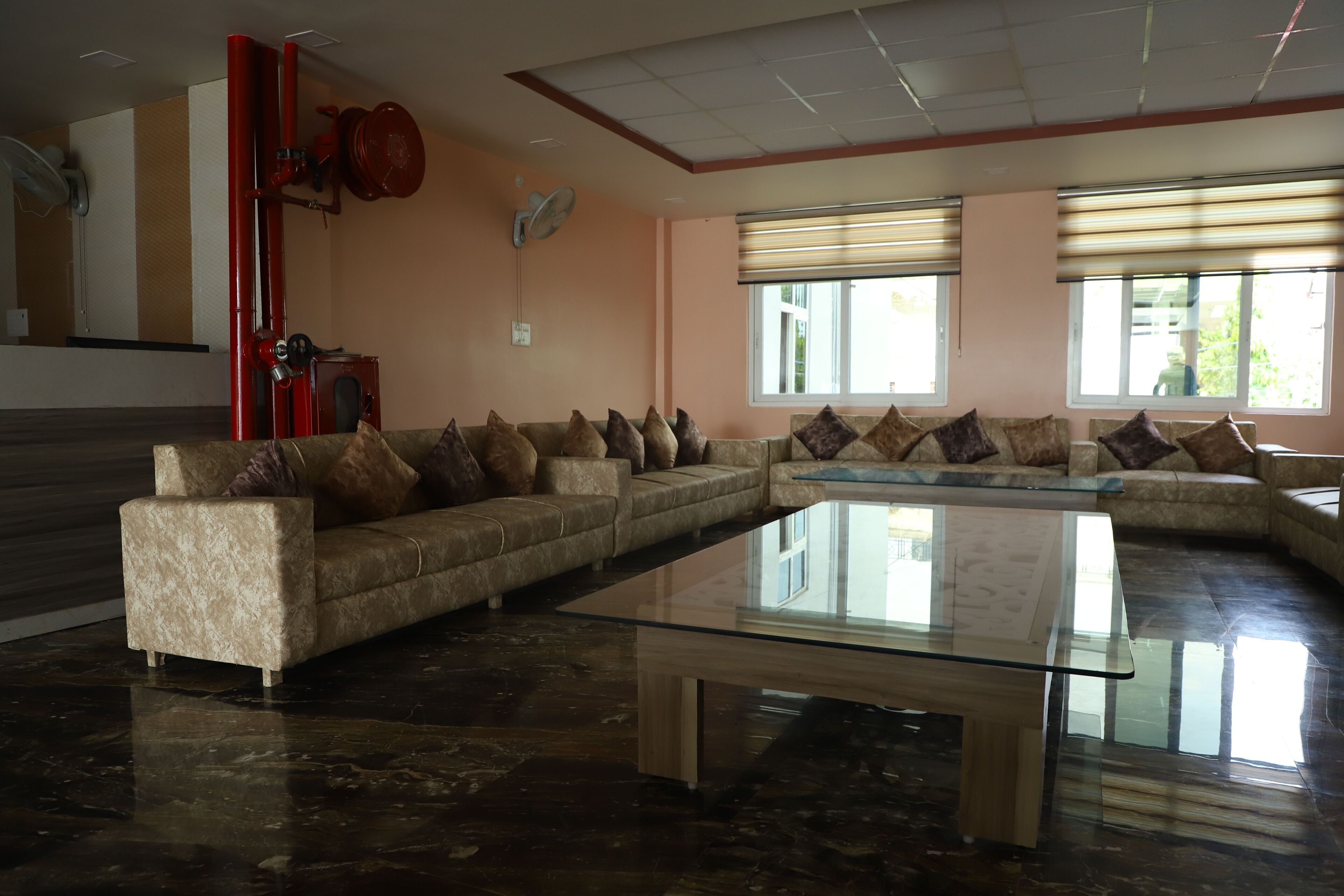 A spacious living room with a large sectional sofa, a glass coffee table, and a red fire extinguisher mounted on the wall.