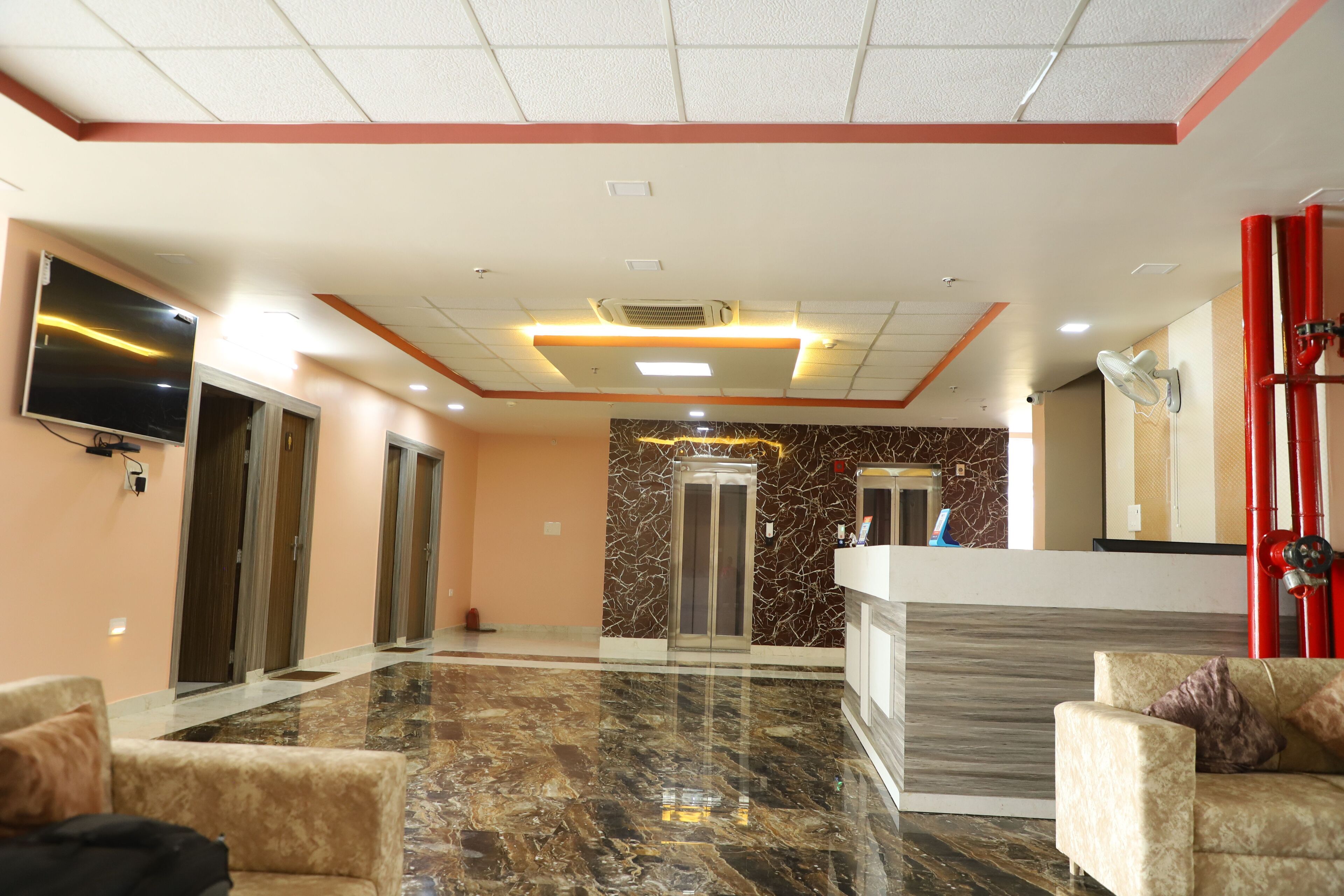 A hotel lobby with a marble floor, a reception desk, and a TV mounted on the wall.