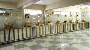 Un área de recepción de hotel con piso a cuadros, pared de mármol con diseño de piedra y varias mostradoras de recepción doradas con paneles de vidrio.