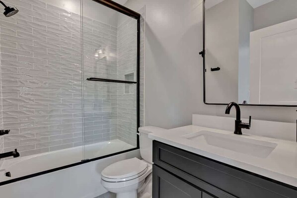 A modern bathroom with a glass shower enclosure, a white toilet, a sink with a black faucet, and a mirror above the sink.