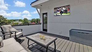 Uma varanda com área de estar externa, uma televisão na parede e vista para a paisagem.