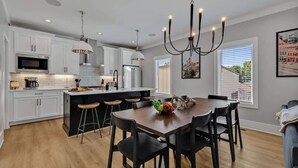 Cozinha moderna com armários brancos, uma ilha central, banquetas e um lustre.