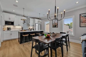 A modern kitchen with white cabinets, a central island, bar stools, and a chandelier. - Tenor - Private Rooftop - Mins to Broadway & 12 S (Nashville)