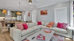 A modern living room with a sectional sofa, a coffee table, and a dining area with a kitchen in the background. - Alto- Lrg Private Rooftop- Mins to Broadway & 12 S (Nashville)