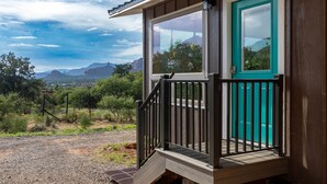 Een houten hutje met een turquoise deur en een balkon met uitzicht op een bergachtig landschap.