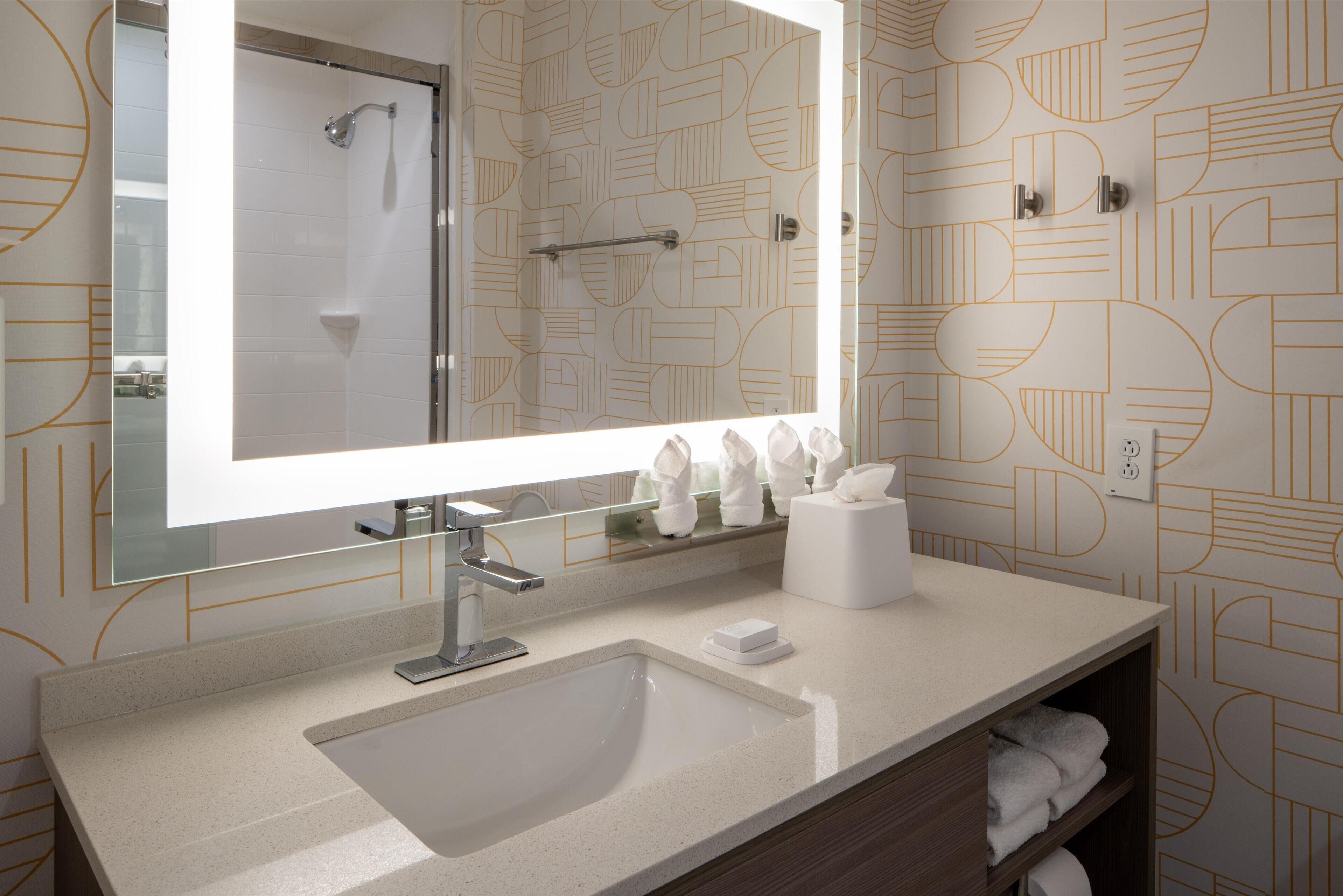A modern bathroom with a large mirror, a sink, and a towel rack.