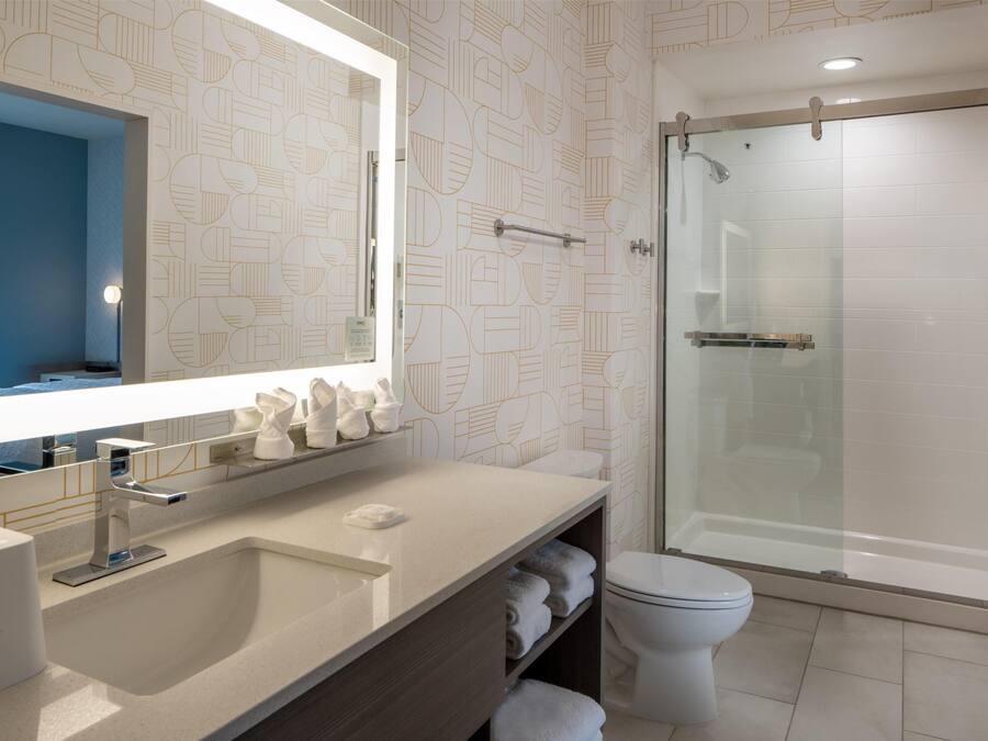 A modern bathroom with a large mirror, a sink, a toilet, and a glass-enclosed shower.