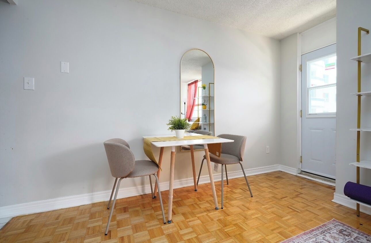 A room with a dining table, two chairs, a mirror, and a bookshelf.