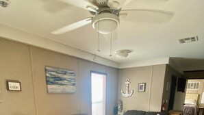 Ein Wohnzimmer mit zwei dunkelgrauen Sofas, einem Couchtisch, einem gemusterten Teppich, einem Deckenventilator und einem Gemälde an der Wand.