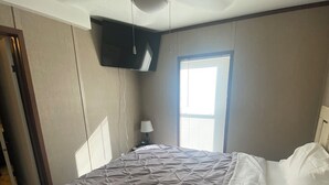 Ein Schlafzimmer mit einem Bett, einem Deckenventilator, einem an der Wand montierten Fernseher und einem Fenster mit Jalousien.