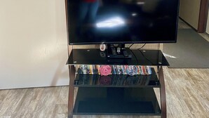 Ein Flachbildfernseher auf einem Glastisch mit Fernbedienung und einem kleinen Lautsprecher.