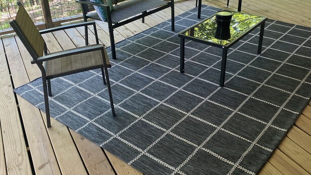 Ein überdachter Außenbereich mit Holzdeck, einem karierten Teppich und zwei Stühlen.