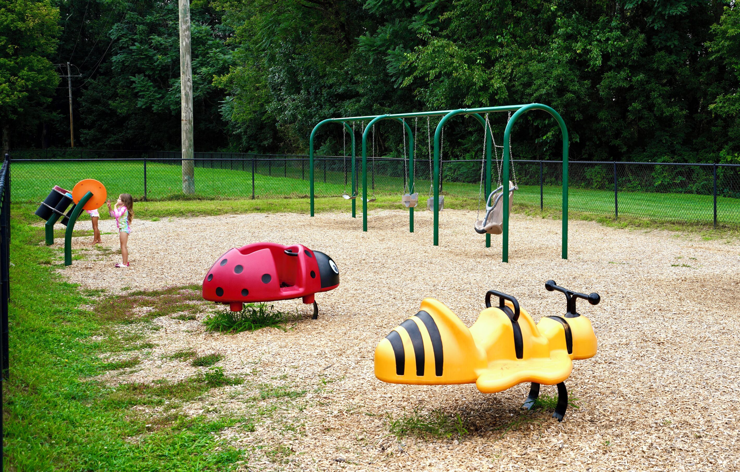 A playground with various play equipment including swings, a slide, and a ladybug-shaped play structure.
