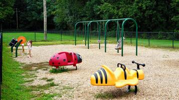 A playground with various play equipment including swings, a slide, and a ladybug-shaped play structure.
