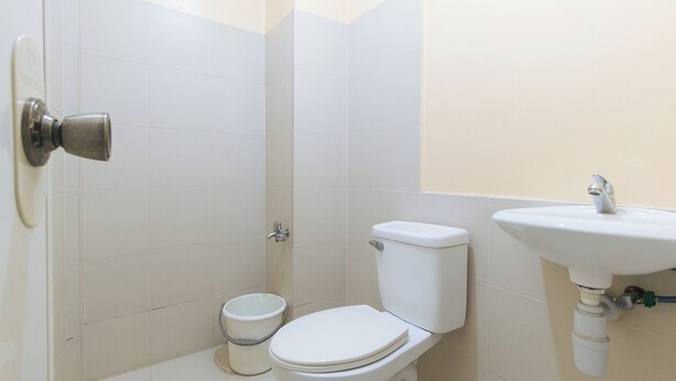 A small, clean bathroom with white tiles, a toilet, a sink, and a toilet paper holder. - Mervin's Terraces By Reddoorz (Manila)