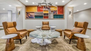 Un área de descanso moderna con sillones de cuero, una mesa de centro de vidrio y un mural abstracto de colores en la pared.