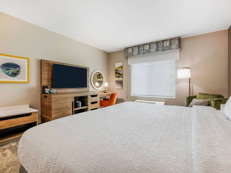 Habitación de hotel con una cama grande, televisión, escritorio con espejo y obras de arte en las paredes.