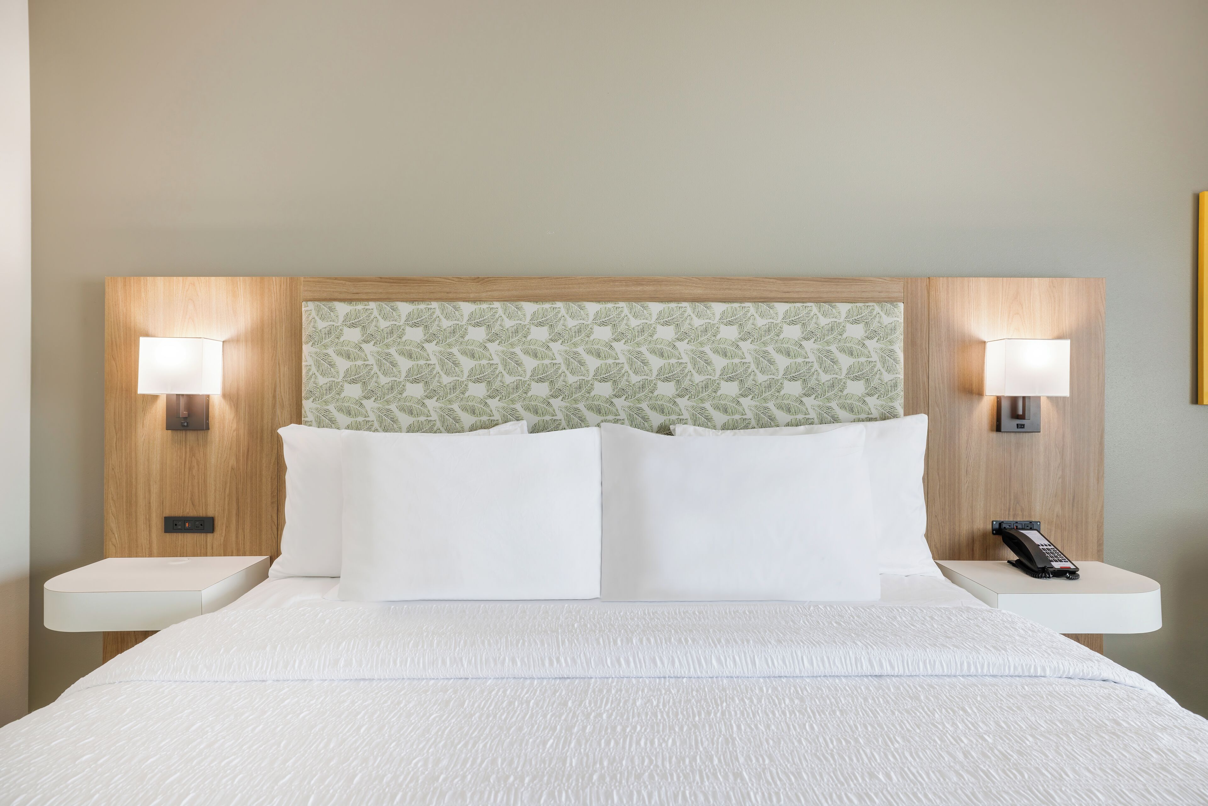 A hotel room with a large bed, two bedside tables, a wall-mounted telephone, and two wall-mounted lamps.