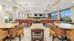 Un comedor moderno con varias mesas y sillas, un banco acolchado verde y amplios ventanales con vistas.