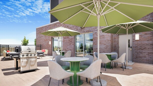 Un patio al aire libre con mesas y sillas redondas, sombrillas verdes y una parrilla.