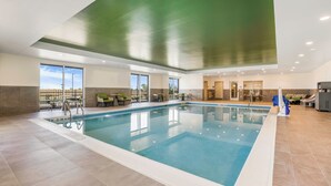 Una amplia piscina interior con agua cristalina, rodeada de sillones de descanso y mesas, y grandes ventanales que ofrecen vistas al exterior.