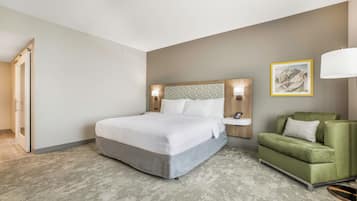 A hotel room with a bed, a green armchair, a nightstand, and a wall-mounted lamp.