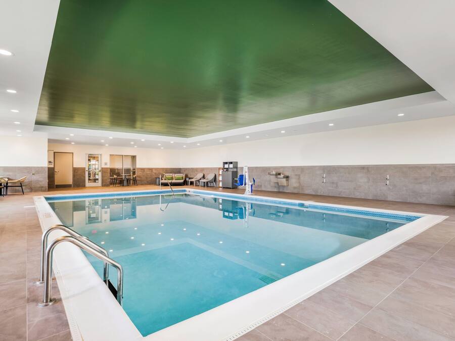 A large indoor swimming pool with a clear blue water surface, surrounded by a tiled floor and walls.