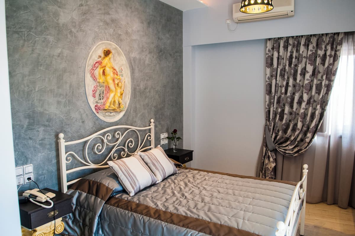 A bedroom with a bed, a nightstand, a wall-mounted air conditioner, and a painting.