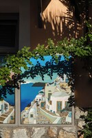 Un cuadro enmarco de un pueblo costero con edificios blancos y puertas azules, sobre un muro de piedra.