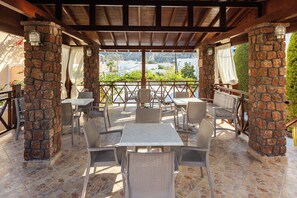 An outdoor patio with stone pillars, wicker furniture, and a view of a mountainous landscape. - Polydefkis Hotel (Santorini)