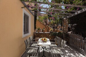 Une terrasse extérieure avec une table et des chaises, entourée de plantes en pot et d’un mur de pierre.