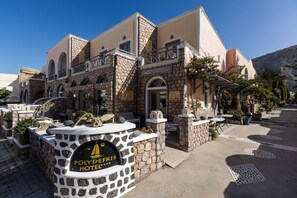 A hotel with a stone facade, outdoor seating, and a sign reading "POLYDEKS HOTEL". - Polydefkis Hotel (Santorini)