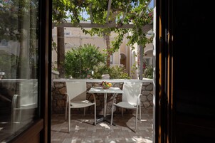 Un patio exterior con una mesa y dos sillas de mimbre, un muro de piedra y vistas a un edificio con arcos.