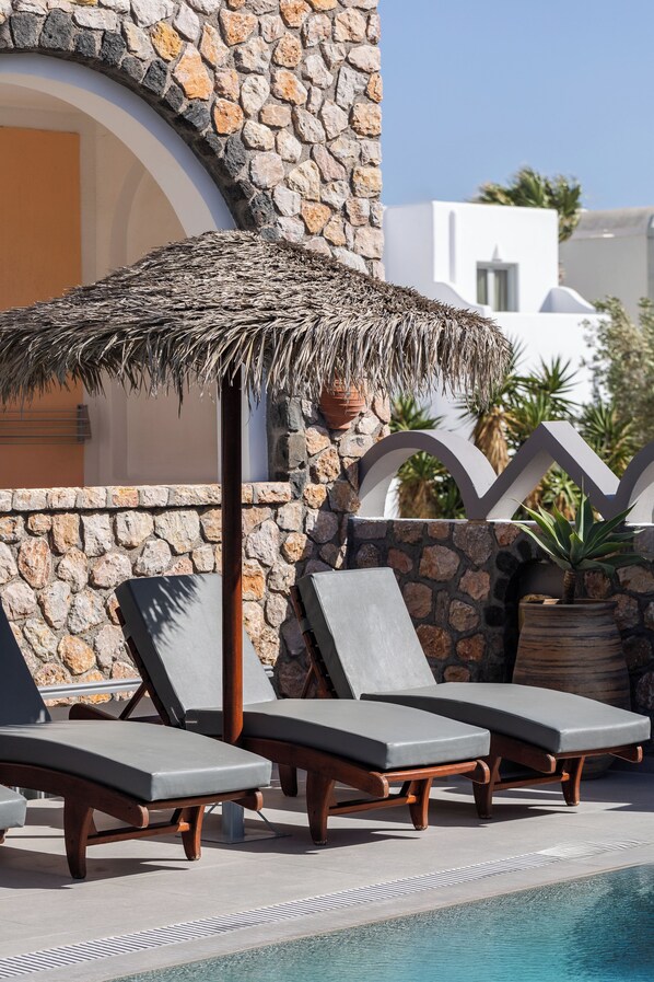 Un espace aménagé au bord de la piscine, avec des chaises longues, un parasol en chaume et un mur en pierre.