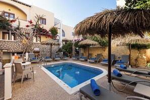 Une piscine entourée de murs de pierre et de plantes, avec des chaises longues et des parasols.